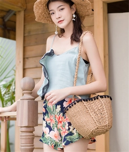 Close-up of straw beach bag with decorative black pom-pom trim and woven handles