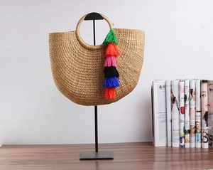 Detail of a semi-circular straw tote bag with vibrant multi-color tassels on a white background
