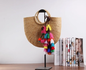 Detail of a semi-circular straw beach bag featuring colorful boho tassels and natural texture