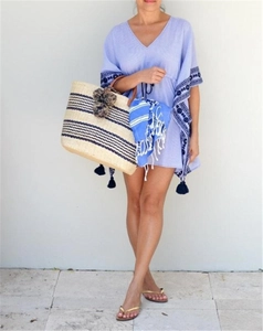 Detail of light blue embroidered kaftan with bohemian tassels and straw tote bag