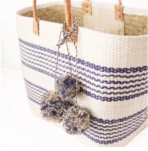 Detail of straw woven beach bag with blue stripes, leather handles and decorative pom-poms