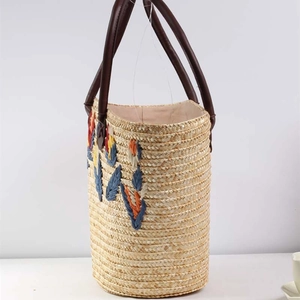 Straw bucket bag with colorful leaf embroidery and brown handles for beach vacations