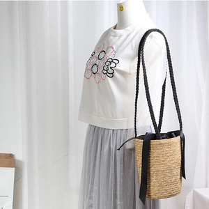 Handwoven straw bucket bag with black bow straps and drawstring closure shown on model