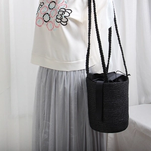 Woven black straw bucket bag with bow detail and braided straps worn on shoulder