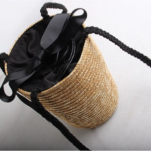 Handcrafted woven straw bucket bag with a black ribbon bow and drawstring closure