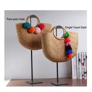 Handwoven straw beach bag with colorful pom-poms and tassels on a display stand