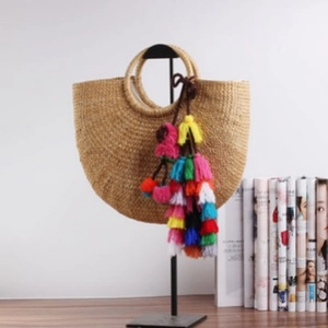 Bohemian half-moon woven straw handbag with vibrant colorful tassel on display
