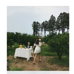 Outdoor view of a white minimalist summer dress and straw bag in an orchard setting