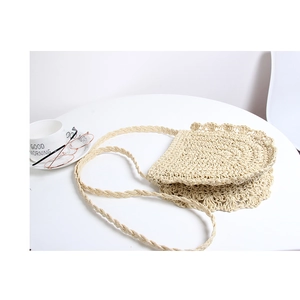 Detail of hand-woven beige straw crossbody bag with scallop edges and braided shoulder strap