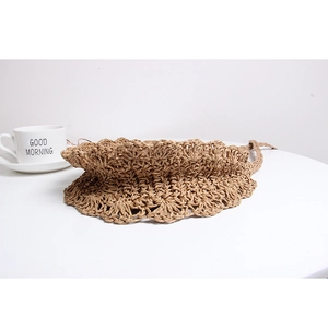 Handcrafted khaki straw hat with scalloped wavy edges placed on a white table