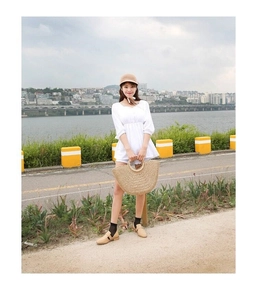 Close-up of semi-circular straw handbag paired with white puff sleeve top and summer hat