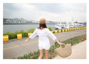 Back view of woman with round straw handbag and sun hat at a scenic coastal harbor
