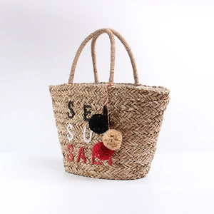 Detail of straw tote bag with Sea Sun Salt embroidery and colorful pom-pom decor