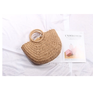 Detail view of a semi-circular straw woven handbag on white fabric for summer vacations