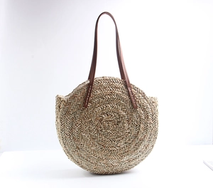 Macro detail of hand-woven round straw tote bag with brown leather handles and inner lining