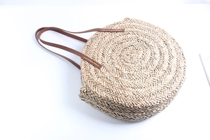 Close-up of a circular straw woven beach bag featuring durable dark brown shoulder straps