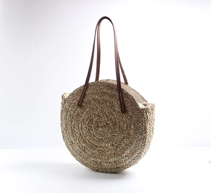 Detail of hand-woven straw beach bag featuring brown leather straps and sturdy stitching