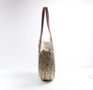 Detail of hand-woven straw tote bag showing brown leather handles and metal zipper closure