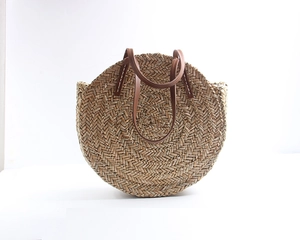 Detail of round straw bag with natural fiber weave and brown leather shoulder straps
