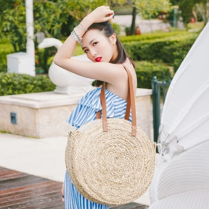 Detail of round straw beach bag with woven texture and brown leather shoulder straps