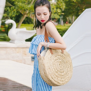 Close-up of circular straw beach bag with brown leather handles and natural fiber weaving
