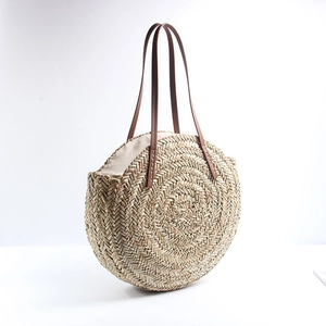 Natural round straw beach bag with brown leather handles and bohemian woven texture