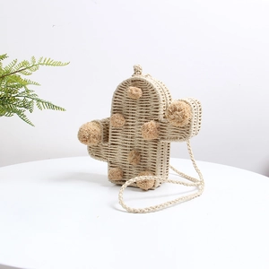 Nahaufnahme einer kaktusförmigen Strohtasche mit dekorativen Pompons auf einem Tisch