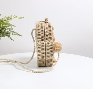 Detail einer runden Stroh-Strandtasche mit dekorativen Pompons und dünnem Schulterriemen