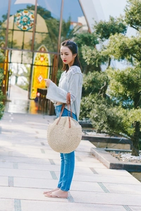 Outdoor model shot of a large round straw tote bag with brown leather shoulder straps