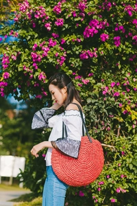 Detail of red circular straw bag with fine concentric weave and black leather strap