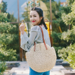 Detail of handwoven round straw tote bag with brown leather strap and white stitching