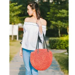 Detail of a round coral straw woven bag with a black leather strap on a model