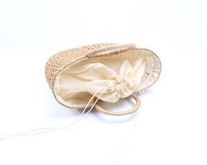 Detail of handmade woven straw tote with hollow design and cream drawstring lining