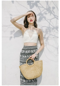 Fashionable semi-circle straw handbag held by a model with a bohemian holiday outfit