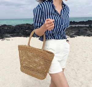 Detail of hand-woven hollow straw tote bag with round handles on a sunny summer beach