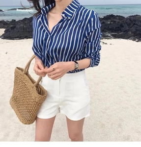 Close-up of a woven straw beach tote styled with a striped shirt and white shorts for summer