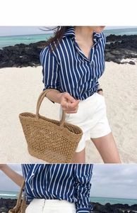Detail of a chic woven straw tote bag paired with a striped shirt on a sunny summer beach
