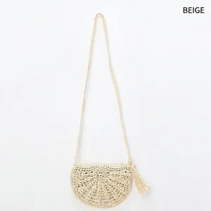 Detail of beige handmade straw crossbody bag with decorative tassels and woven texture