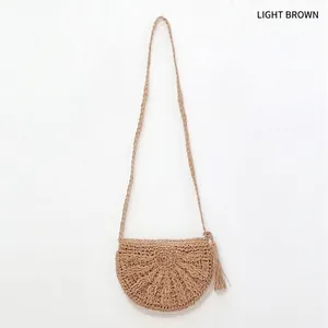 Detail of light brown semi-circle straw crossbody bag with decorative tassels and woven texture