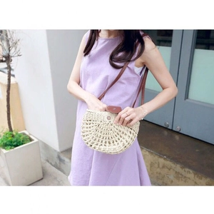 Detail of hollow woven straw bag with dark brown leather strap on a purple dress