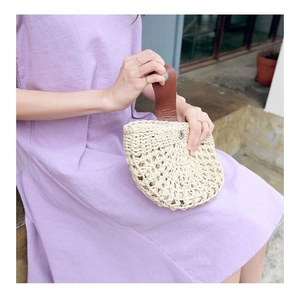 Detailed view of handmade straw handbag with hollow texture and brown leather strap