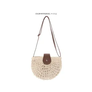 Detail of beige semi-circular woven straw bag with brown leather flap and strap