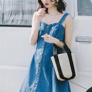 Detail of straw woven bucket bag with black ribbon handles held by a model in denim dress
