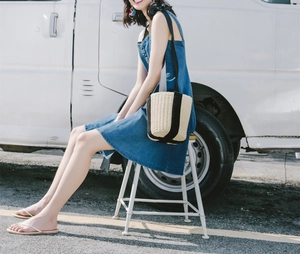 Detail of straw bucket bag with black straps on a model in a summer outdoor setting