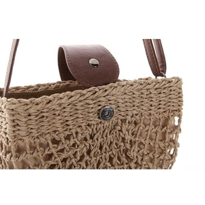 Close-up of handmade straw woven bag showing leather cover and magnetic metal buckle