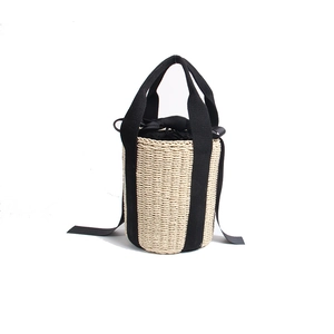 Beige straw bucket bag with black canvas handles and decorative ribbon on white background