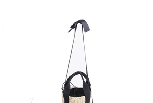 Detail of straw bucket bag featuring black ribbon handles and elegant bow strap