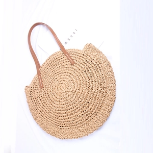 Close-up of circular straw bag with brown leather handles and reinforced white stitching