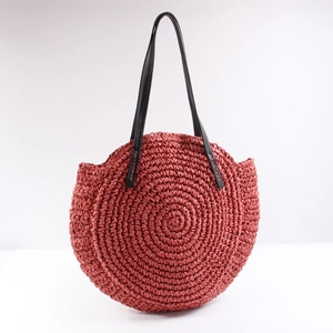 Large round rust red woven straw shoulder bag with black leather straps for beach vacation