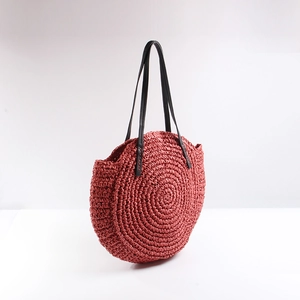 Detail of round straw beach bag in brick red with woven texture and black straps